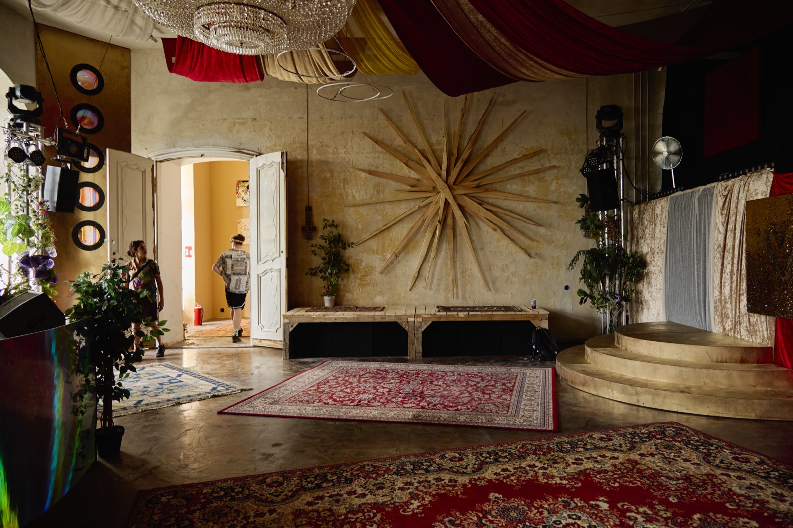 Ein Ausstellungsraum im Schloss mit einer großen Sonnenskulptur aus Holzstäben und Teppichen.